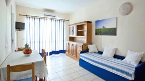 A room with a dining table, chairs, a sofa, a TV, and a cabinet. - Golfo Aranci Stay at Baia de Bahas (Golfo Aranci)