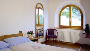 Un dormitorio con cama, una silla, un ventanal y un radiador.