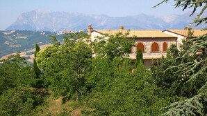 Un edificio con techo de tejas y ventanas de arco, rodeado de abundante vegetación y montañas al fondo.