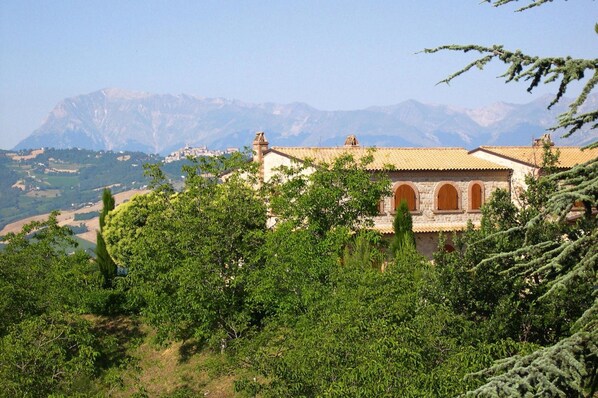 A building with a tiled roof and arched windows, surrounded by lush greenery and mountains in the background.