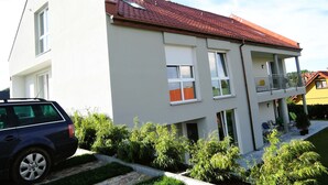 Moderni, kaksikerroksinen talo, jossa on punatiilinen katto, valkoiset ulkoseinät ja parveke, jossa on kaide.