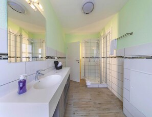 Un bagno moderno con un grande specchio, due lavandini, una doccia e pavimento piastrellato.