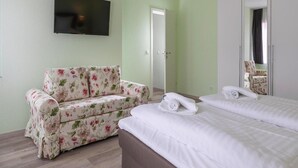 Une chambre d’hôtel avec un canapé à motifs floraux, un lit avec du linge de maison blanc, un téléviseur à écran plat fixé au mur et une armoire avec un miroir.