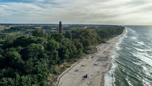 Oversigtsbillede af en strand med et fyrtårn, frodigt grønt og en klar himmel.