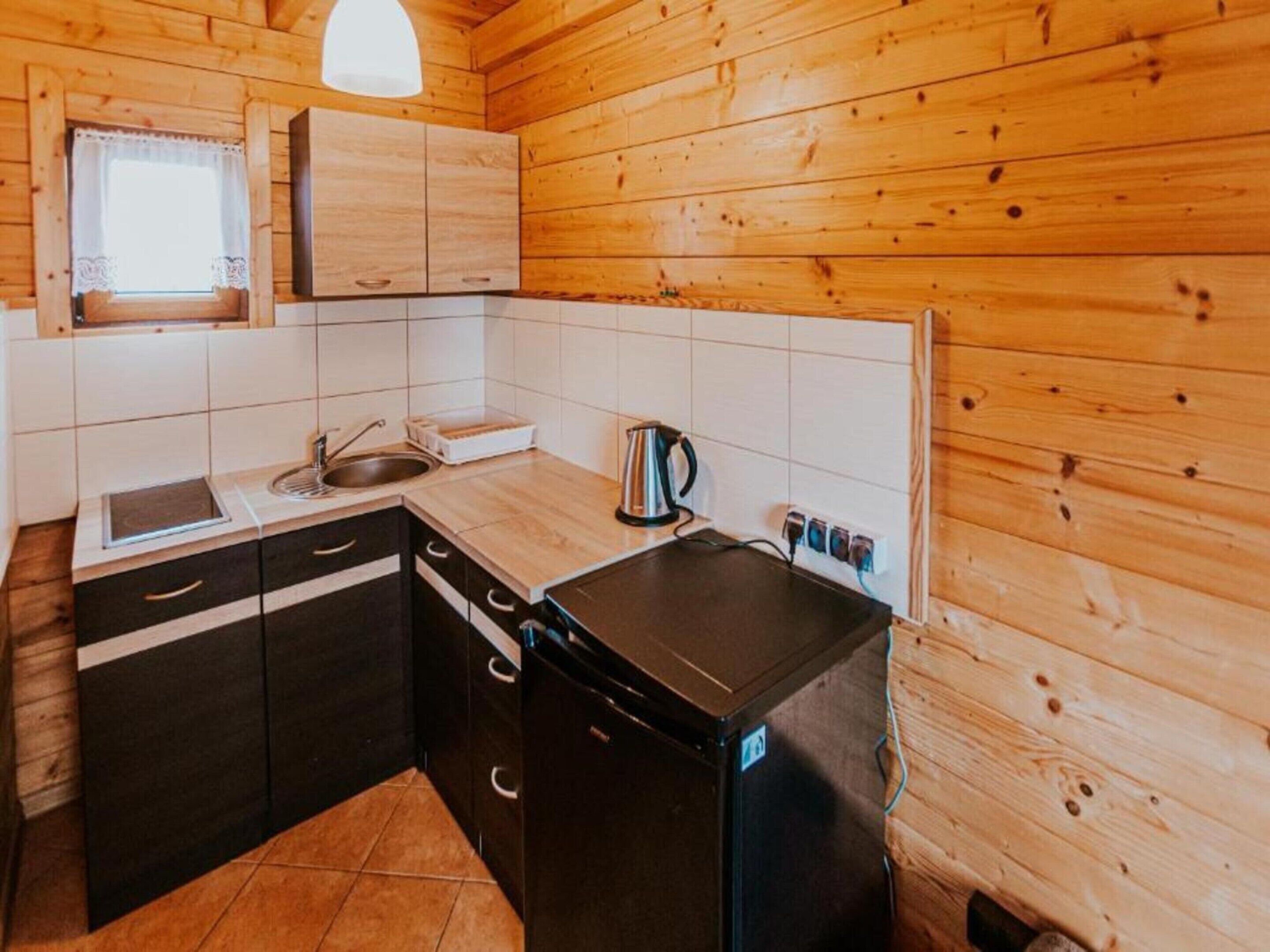 A compact kitchen with wooden walls, a black refrigerator, a sink, and a window with a curtain.