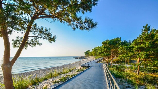 A pathway along a beach with a metal railing, sandy beach, and trees.