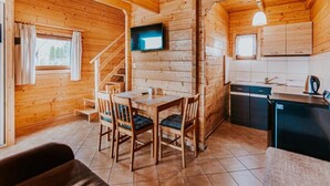 A cozy cabin with a wooden interior, a dining area with chairs and a table, a kitchen with a sink and cabinets, and a staircase leading to another level.