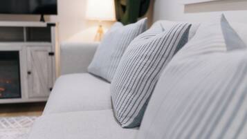 Een witte bank met gestreepte kussens, een televisie en een lamp in een woonkamer.