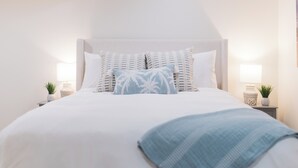 Un lit bien fait, avec une tête de lit blanche, deux tables de chevet avec des lampes et des coussins décoratifs.