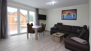 A modern living room with a sofa, a coffee table, and a dining table with chairs. There is a TV mounted on the wall and a painting above the sofa. - Appartement Hafenflair am Plauer See (Plau am See)
