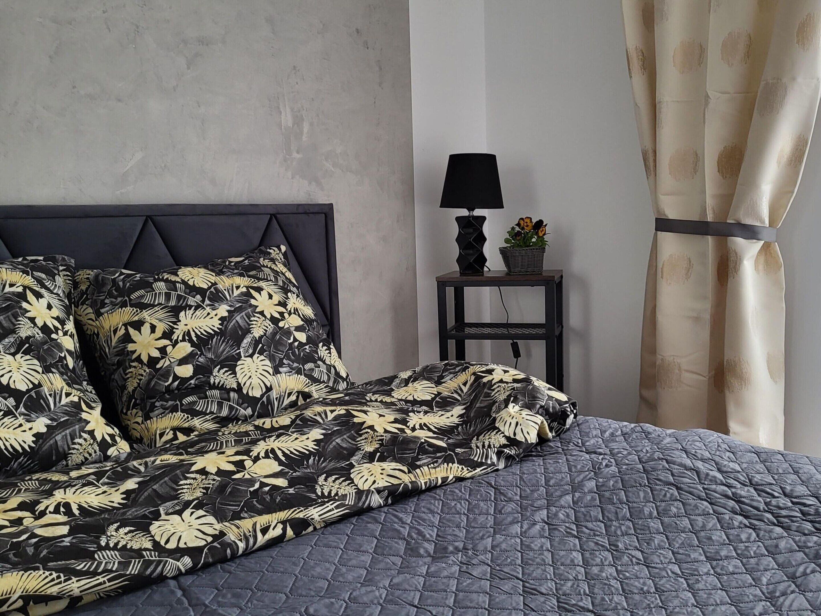 Une chambre à coucher avec un lit, une table de chevet, une lampe et un rideau.