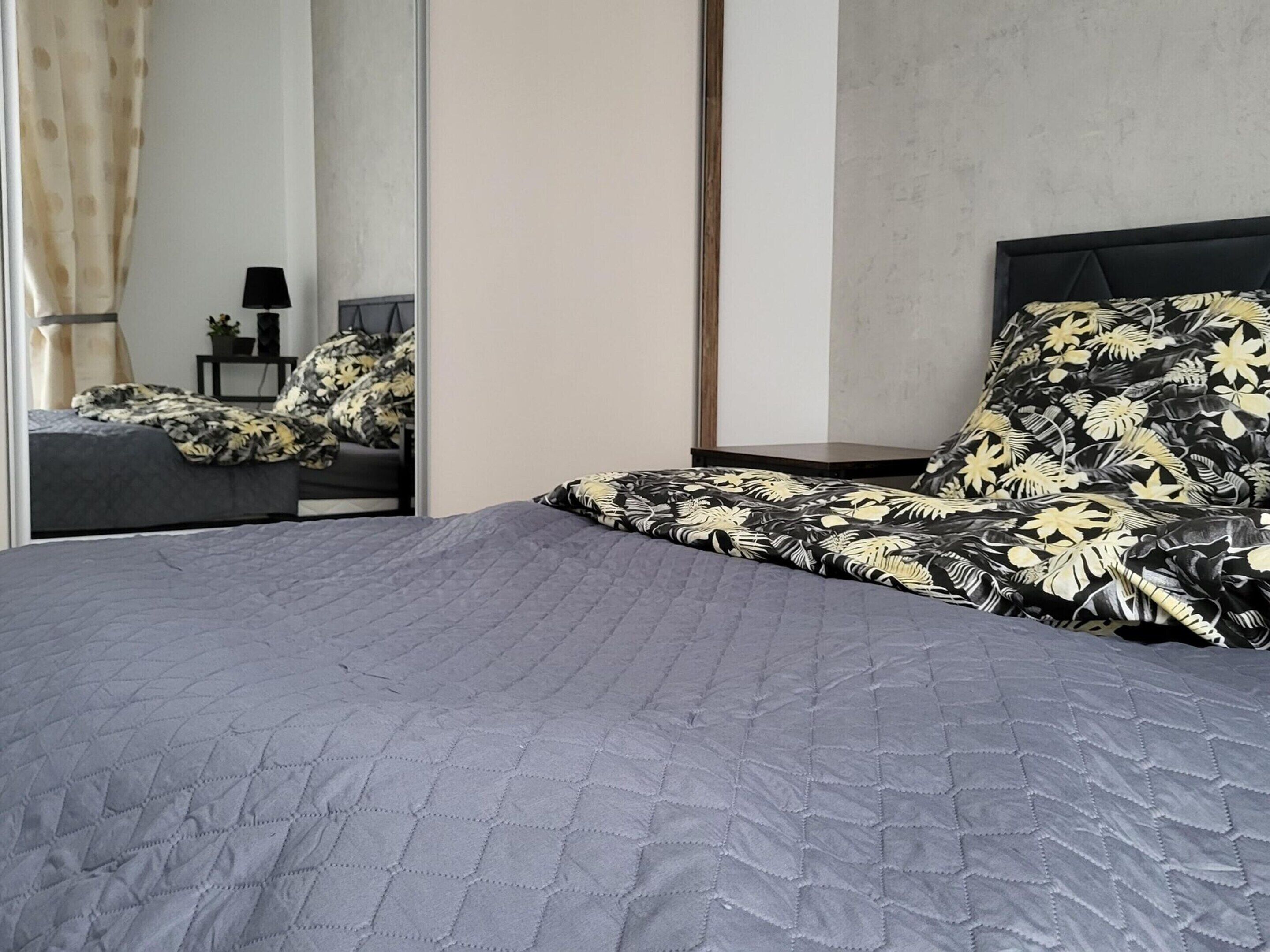 A modern bedroom with a large bed, a nightstand, a mirror, and a view of a bathroom.