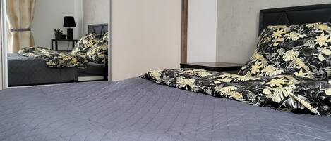 A modern bedroom with a large bed, a nightstand, a mirror, and a view of a bathroom.