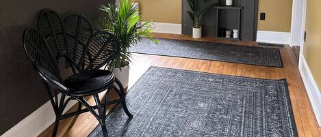 Una habitación con una pared oscura, una ventana, una chimenea, una silla negra y una alfombra estampada.
