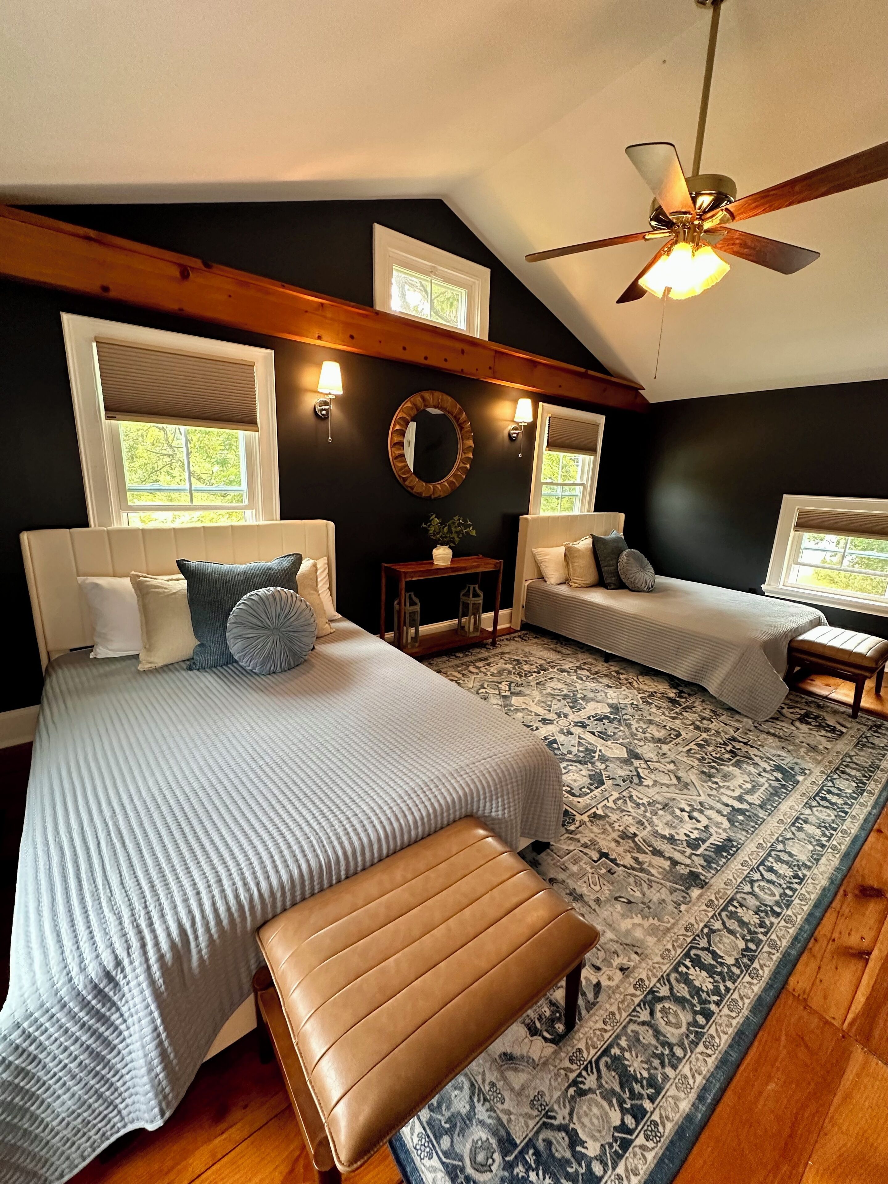 A bedroom with two beds, a ceiling fan, and a large rug.