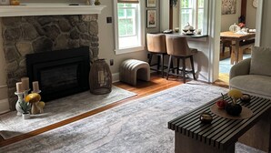 A living room with a stone fireplace, a flat-screen TV, a coffee table, and a dining area with a wooden table and chairs. - Spacious 7 bedroom house, Near jiminy Peak  in Hancock ma , In the Berkshires (New Lebanon)