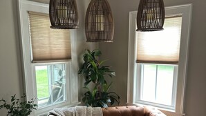 A cozy living room with a brown leather sofa, two wicker pendant lights, a potted plant, and a window with blinds. - Spacious 7 bedroom house, Near jiminy Peak  in Hancock ma , In the Berkshires (New Lebanon)