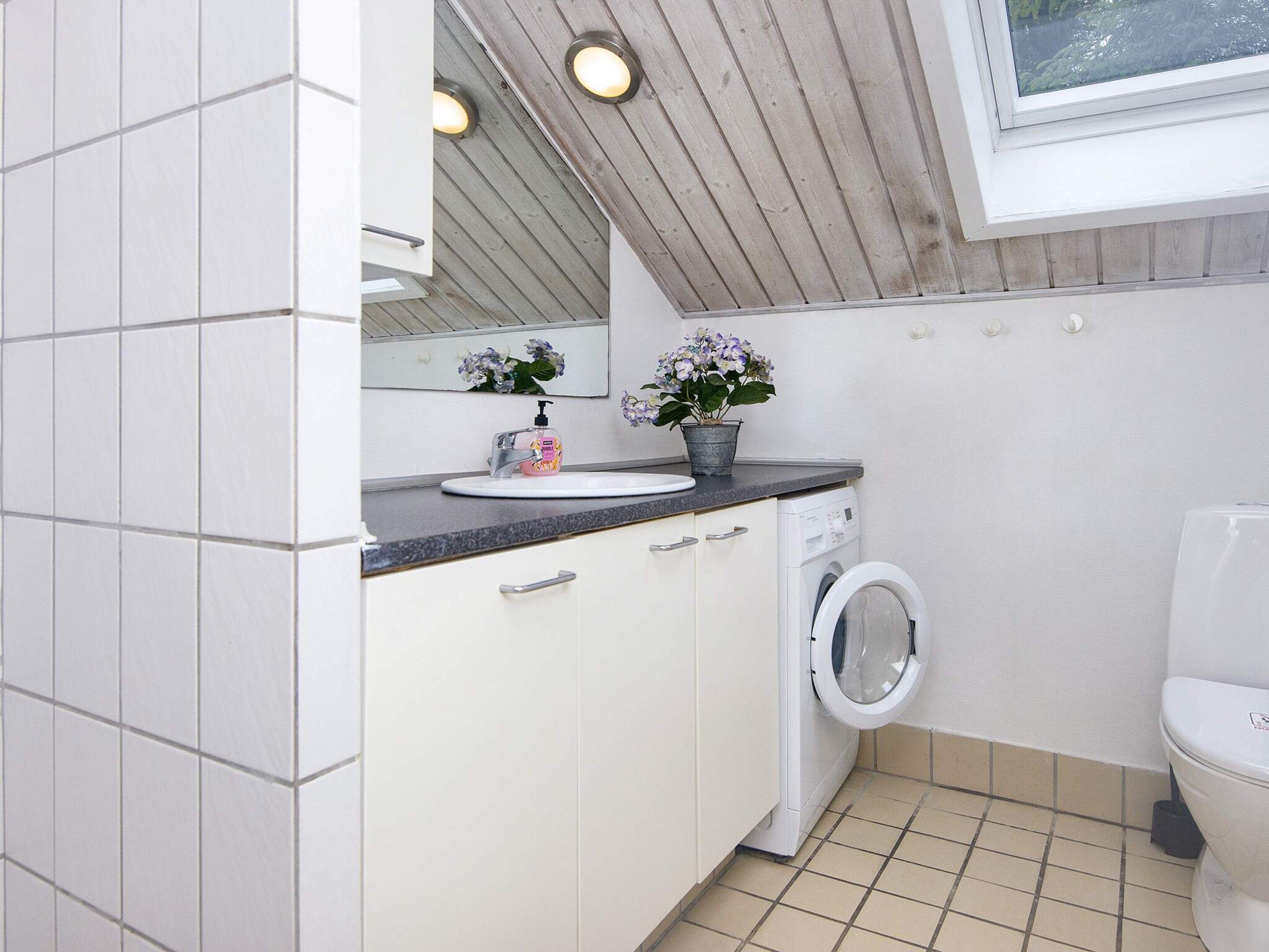 A compact bathroom with a washing machine, a toilet, and a sink with a mirror above it.
