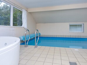 Ein Schwimmbad mit Whirlpool, Fliesenboden und einem Fenster mit Blick auf Bäume.
