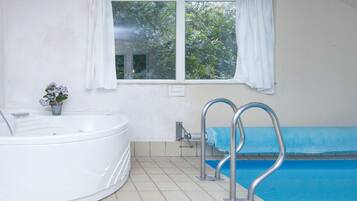 Un baño con bañera, una ventana con cortinas y una piscina con un tapete azul.