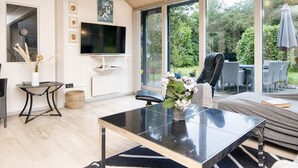 A modern living room with a glass coffee table, a flat-screen TV, and a large window offering a view of the outdoors. - 8 Person Holiday Home in Oksbol (Oksbol)