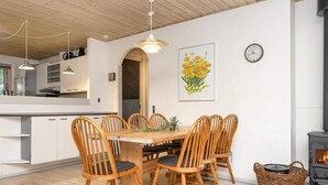 A dining area with a wooden table and chairs, a clock on the wall, and a fireplace. - 8 Person Holiday Home in Oksbol (Oksbol)