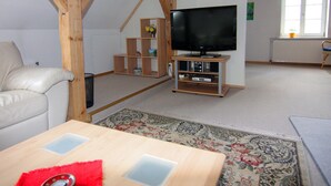 A living room with a television on a wooden stand, a white leather sofa, and a patterned rug.