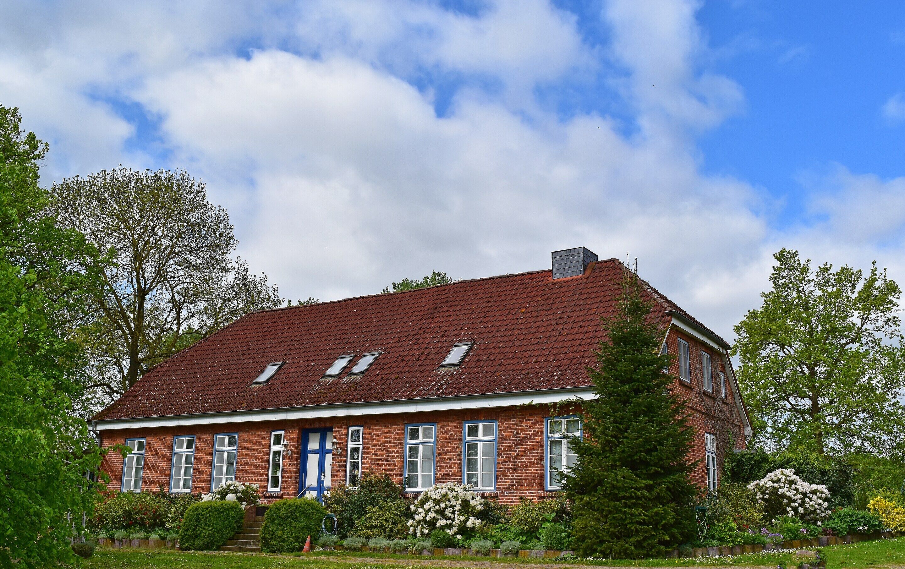 A red brick house with a sloped roof, multiple windows, and a blue door.