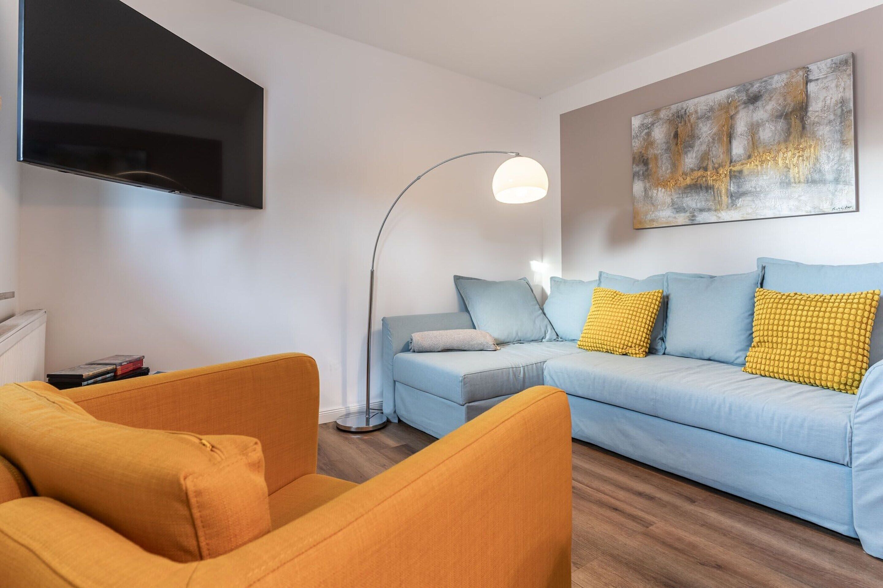 A living room with a sofa, armchairs, a TV, a floor lamp, and a painting on the wall.