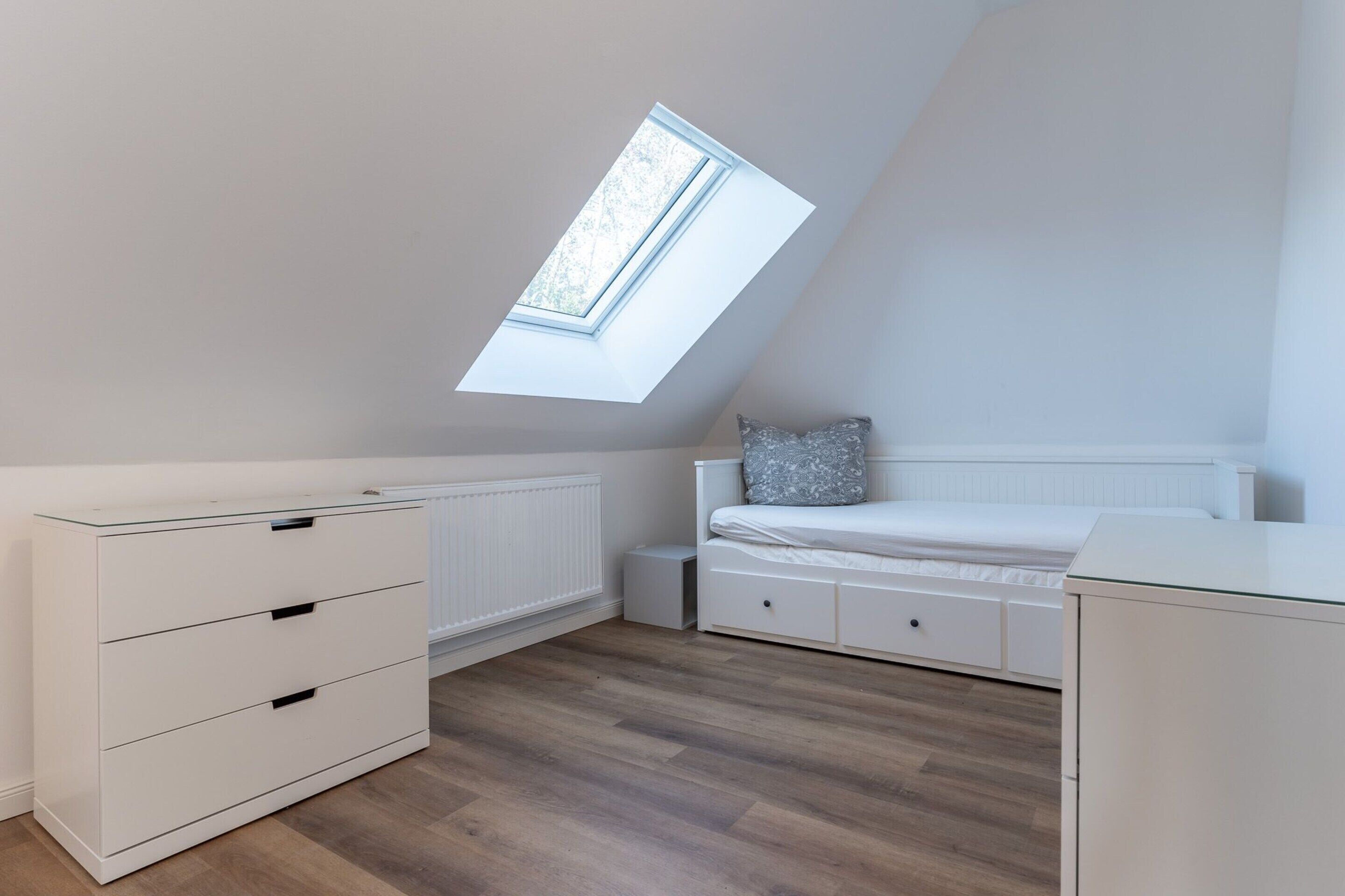 Een slaapkamer met een schuine kap, dakraam, bed, linnenkast en een radiator.