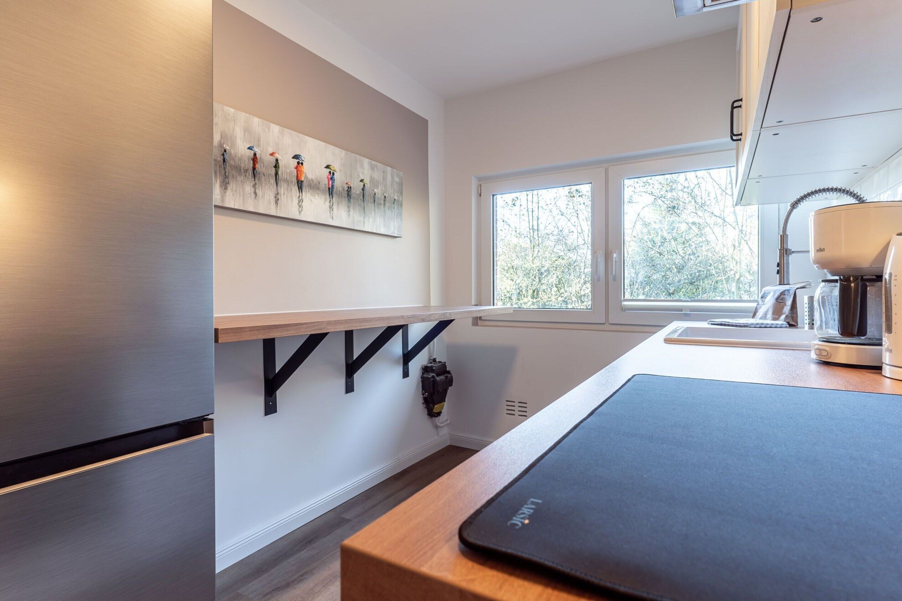 Una cocina moderna con un refrigerador de acero inoxidable, una encimera de madera, una cafetera y una ventana con vistas a árboles.