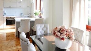 A modern kitchen with white cabinets, a dining area with a glass table, and a vase of flowers. - Holiday Home Near Baltic Sea Beach (Międzyzdroje)
