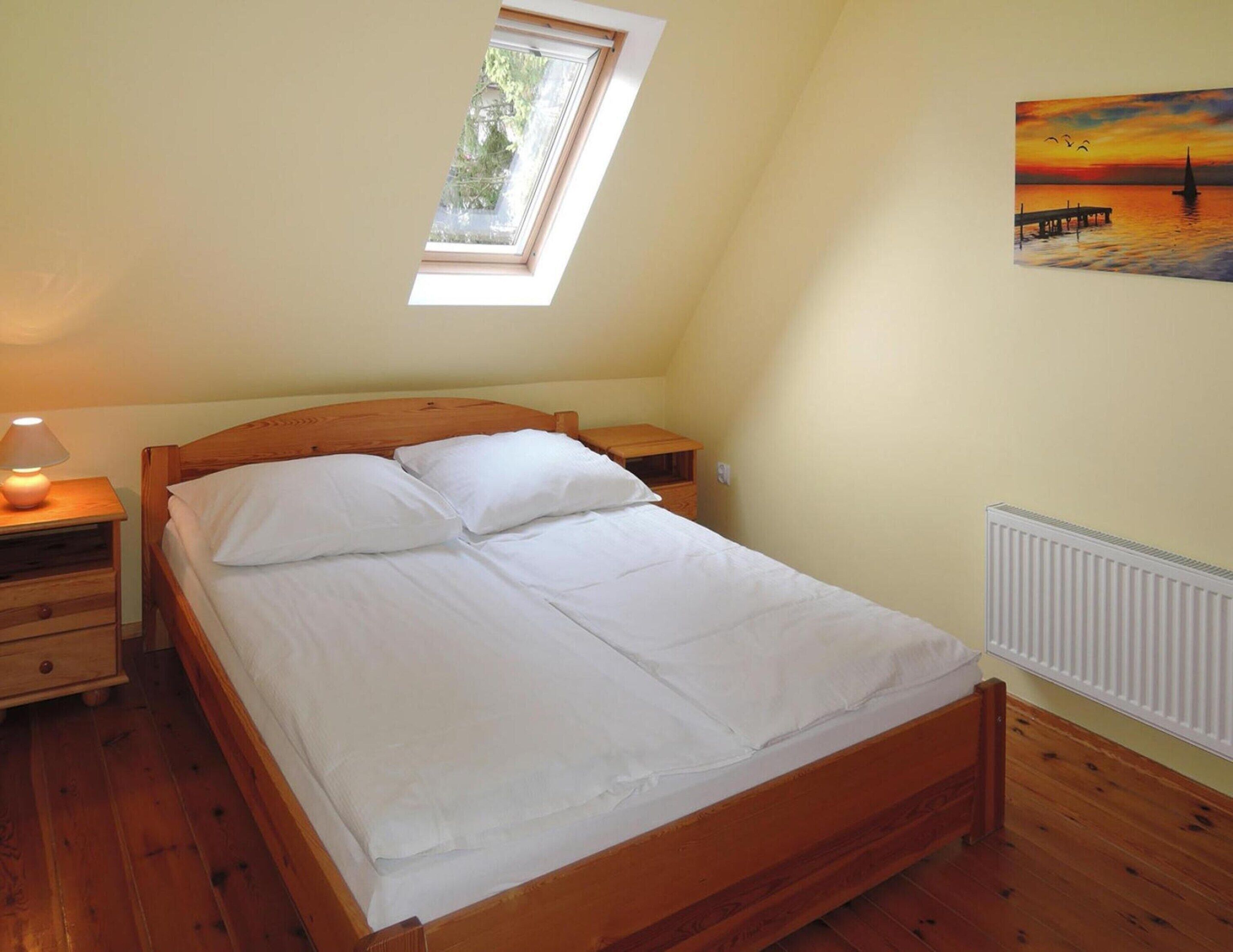 A bedroom with a wooden bed, a nightstand, a lamp, a window, and a painting on the wall.