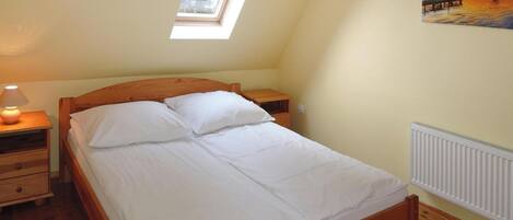A bedroom with a wooden bed, a nightstand, a lamp, a window, and a painting on the wall.