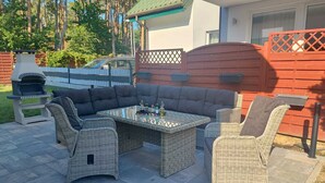 An outdoor patio with wicker furniture, a glass-top table, and a brick oven. - Holiday Home in Lukecin Near Baltic Sea (Dziwnów)