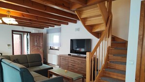 A living room with a sofa, a coffee table, a TV, and a wooden staircase. - Holiday Home in Lukecin Near Baltic Sea (Dziwnów)