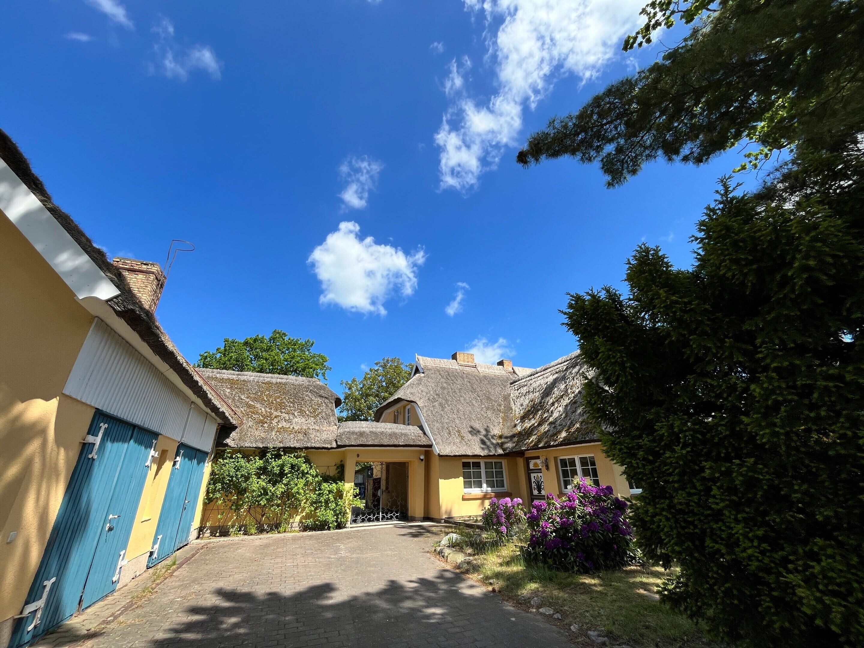 A traditional building with a thatched roof, a paved driveway, and a small garden with purple flowers.