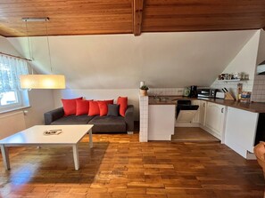 A compact living space with a sofa, a dining table, a kitchen area with a microwave, and a window with curtains.