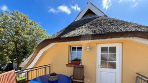 A thatched-roof house with a wooden deck, a round table, and two chairs. - Ferienwohnung, Wieck am Darss (Wieck auf dem Darss)