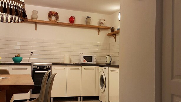 A kitchen with white cabinets, a microwave, a washing machine, and a wooden shelf with decorative items. - Holiday Home by Lake Dejgunek Gizycko (Gizycko)