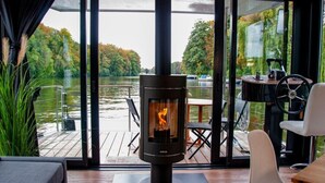 Ett modernt rum med en vedeldad kamin, stora fönster och utsikt över en sjö.
