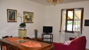 A dining area with a wooden table and chairs, a red sofa, a television on a stand, and two framed pictures on the wall. - Pretty Holiday Home Casa Luca With Above-ground Pool in Capezzano Pianore (Camaiore)