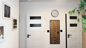 Ein Flur mit weißen Türen, einer Holztür, einer Uhr und gerahmten Bildern an den Wänden.