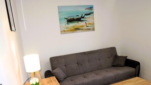 Ein Wohnzimmer mit grauem Sofa, einem Holztisch und einem Gemälde von Booten an der Wand.