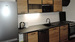 Eine moderne Küche mit Holzschränken, einem Edelstahlkühlschrank, einer Mikrowelle, einem Spülbecken, einem Geschirrspüler und einem Gasherd.