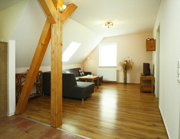 Ett vardagsrum i loftstil med ett sluttande tak, synliga träbjälkar, en soffa, ett soffbord och ett element.