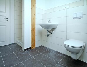 Ein Badezimmer mit einem weißen Waschbecken, einer Toilette und einer Holzwand.