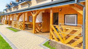 A row of wooden cabins with balconies, a paved walkway, and a covered outdoor area. - Holiday Homes in Miedzyzdroje for 4 People (Międzyzdroje)