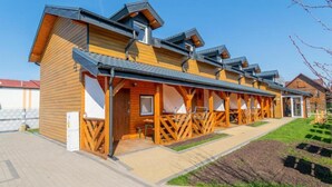 A row of wooden cabins with attached porches, a paved walkway, and a landscaped garden area. - Holiday Homes in Miedzyzdroje for 4 People (Międzyzdroje)