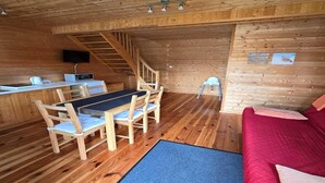 A cozy cabin interior with a wooden dining table, chairs, a red couch, a staircase, and a small kitchenette. - Terraced Home in Sarbinowo Near the Beach (Mielno)